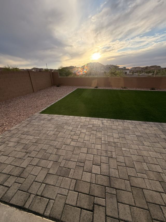 The same paver patio and turf backyard shown in the hero, seen from another angle at sunset.
